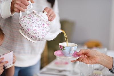 手持白色和粉色花卉陶瓷茶壶的人